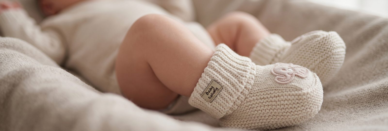 Escarpines tejidos beige de Baby Colloky puestos en los pies de un recién nacido sobre una manta